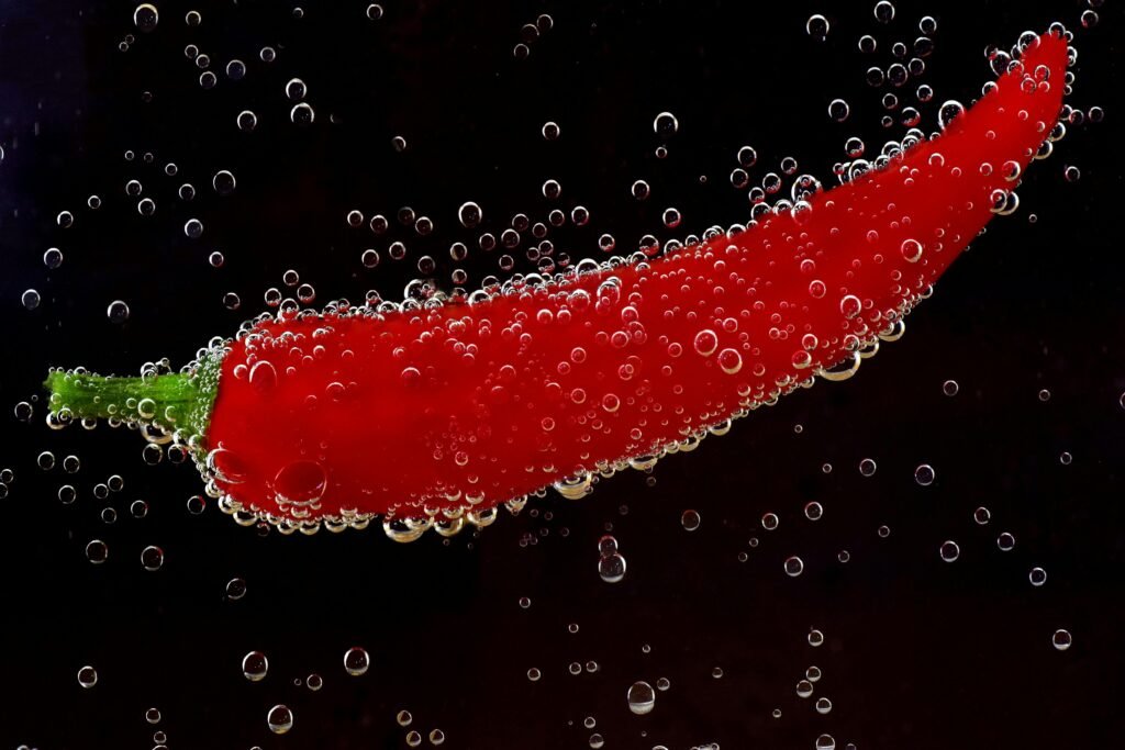 Close-up of a red chili pepper submerged in water with bubbles on a dark background.