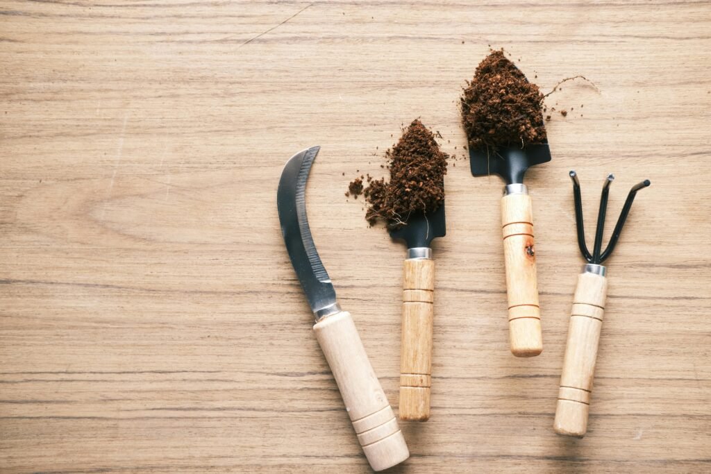 Flat lay of gardening tools on wooden table accompanied by soil.