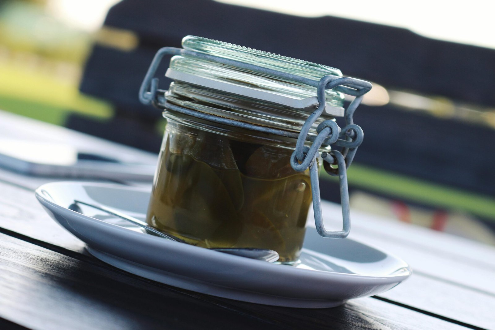 A detailed close-up shot of pickled jalapenos in a glass jar on a white plate outdoors.
